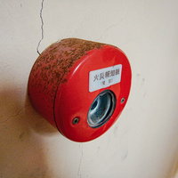 赤い本体が錆びついた劣化した火災報知器の表面の写真