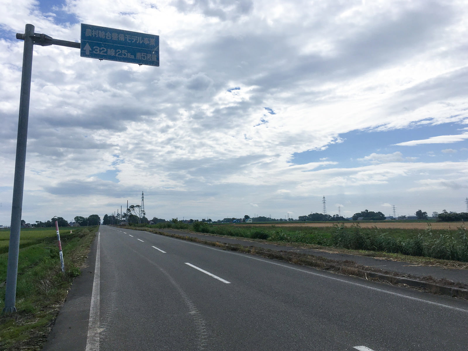 青空の下を一直線に続く農村道路と田園風景