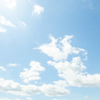 頭上の太陽と澄んだ青空に浮かぶ白い雲の写真