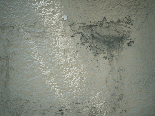 白い塗装が剥がれてコンクリートが露出した老朽化した壁