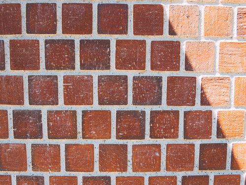 正方形のレンガタイルに斜光が当たる壁面のテクスチャ