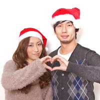 クリスマスにサンタ帽をかぶり指でハートの形を作る恋人の写真