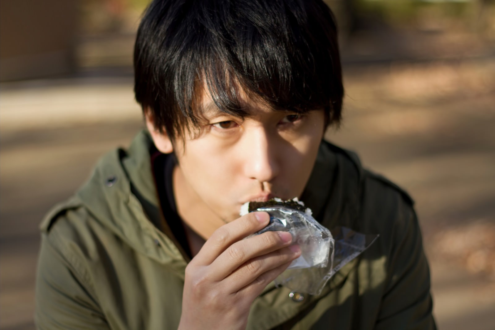 ベンチでおにぎりを食べる孤独な男性［モデル：大川竜弥］