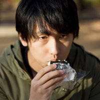 外のベンチでコンビニおにぎりを一人で食べる孤独な男性の写真