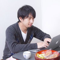 こたつのテーブルの上にノートPCを置いて操作する冬の男性の写真