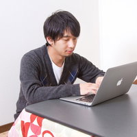 こたつの上にノートPCを置いて寒い日に作業する男性の写真