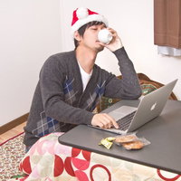 クリスマスにこたつでPCを開いて寂しく過ごすクリぼっちの男性の写真