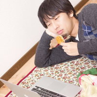 横になりながらノートパソコンの画面を見る男性の写真