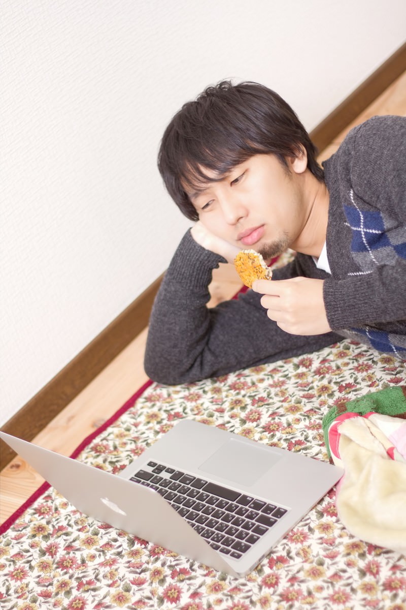 横になってノートPCを見る男性［モデル：大川竜弥］