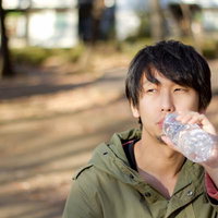 公園のベンチで寂しくペットボトルの水を飲む一人の男性の写真