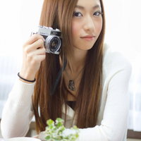 レトロなフィルムカメラを両手で構えるおしゃれな女性の写真
