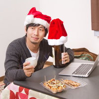 クリスマスにこたつでひとりグラスを傾けて晩酌する男性の写真