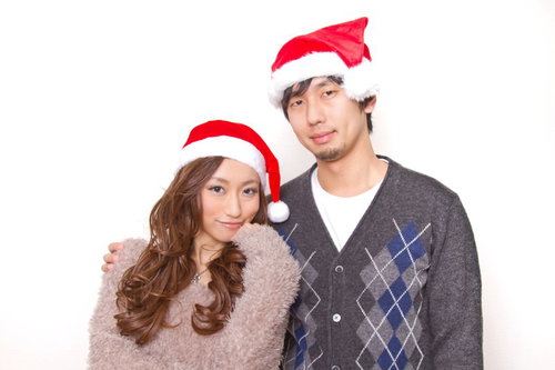 ペアのサンタ帽をかぶってくっつく笑顔の恋人カップル
