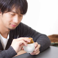 お茶の入った湯呑みにせんべいを浸してふやかす男性の写真