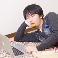 こたつに寝転びながらノートパソコンを操作する冬の男性の写真