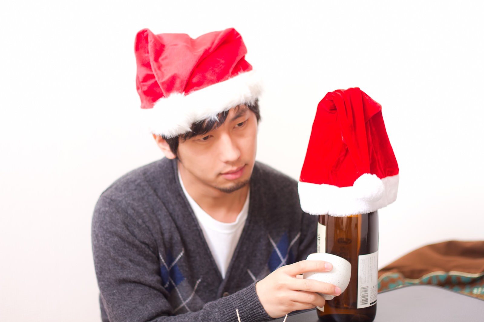 サンタ帽を被りひとりで瓶を持ち上げるクリぼっちの男性［モデル：大川竜弥］