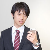 スマホの画面を見て目を見開いて驚くサラリーマンの表情の写真