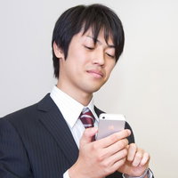 口元がニヤニヤしながらスマホ画面を覗き込むサラリーマンの写真