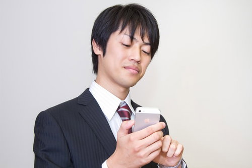 口元がニヤニヤしながらスマホ画面を覗き込むサラリーマン
