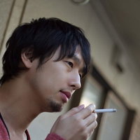 夜のベランダの手すりにもたれて煙草を吸う男性の後ろ姿の写真