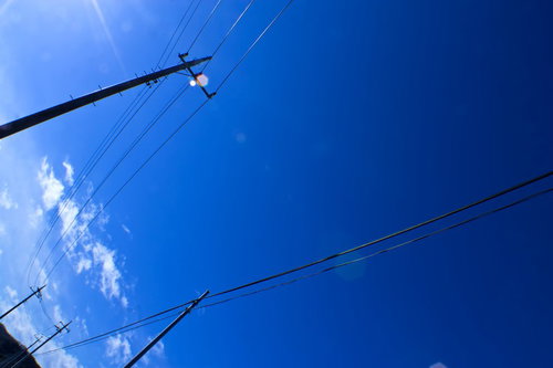 晴れた青空を背景に電線が伸びる電柱の見上げた風景