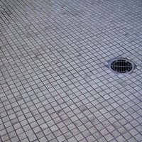 黒ずんだ汚れが染みついたタイルの床と排水口の写真