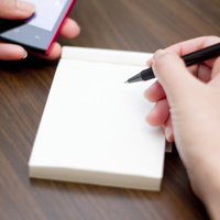 携帯電話の画面を見ながらもう片方の手でメモを取る男性の写真