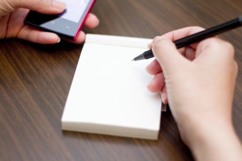 携帯電話の画面を見ながらもう片方の手でメモを取る男性