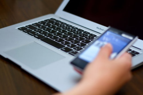 ノートパソコンを開きながらもう片方の手で携帯電話を持つビジネスマン