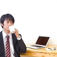 オフィスのデスクでコーヒーカップを手に休憩するWebデザイナーの写真