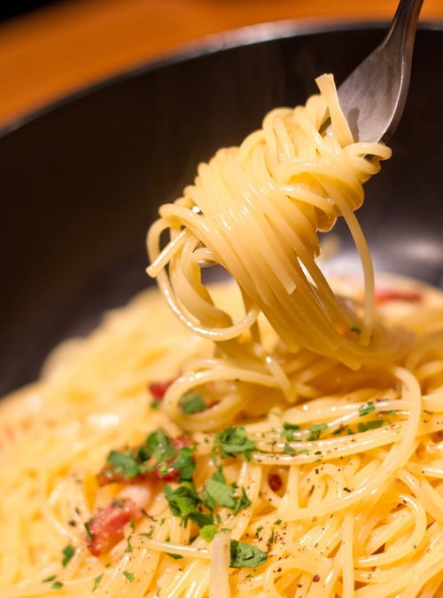 フォークの先にくるくる巻かれたクリーミーなカルボナーラ