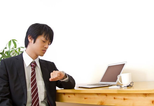 左腕の腕時計を確認するスーツ姿のビジネスマンの手元