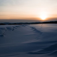 夕焼けのオレンジの空と白い雪原が広がる冬の風景の写真
