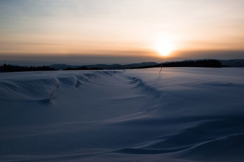 夕焼けのオレンジの空と白い雪原が広がる冬の風景