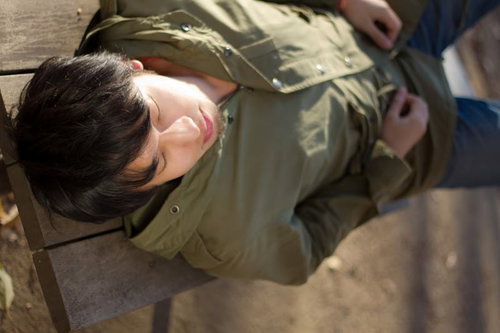 公園のベンチに仰向けで横になってくつろぐ男性