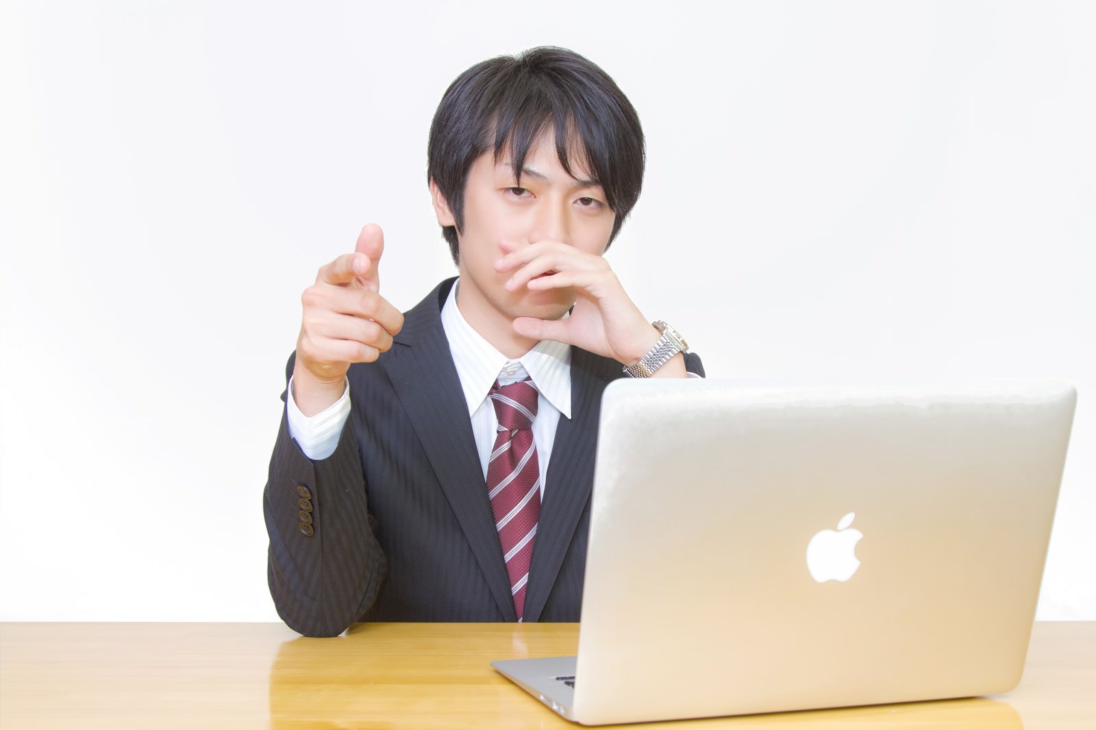 ノートパソコンの前で正面に指を差すスーツ姿の若い男性［モデル：Tsuyoshi.］
