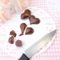 まな板の上でハート型のチョコレートにナイフの刃を当てるの写真