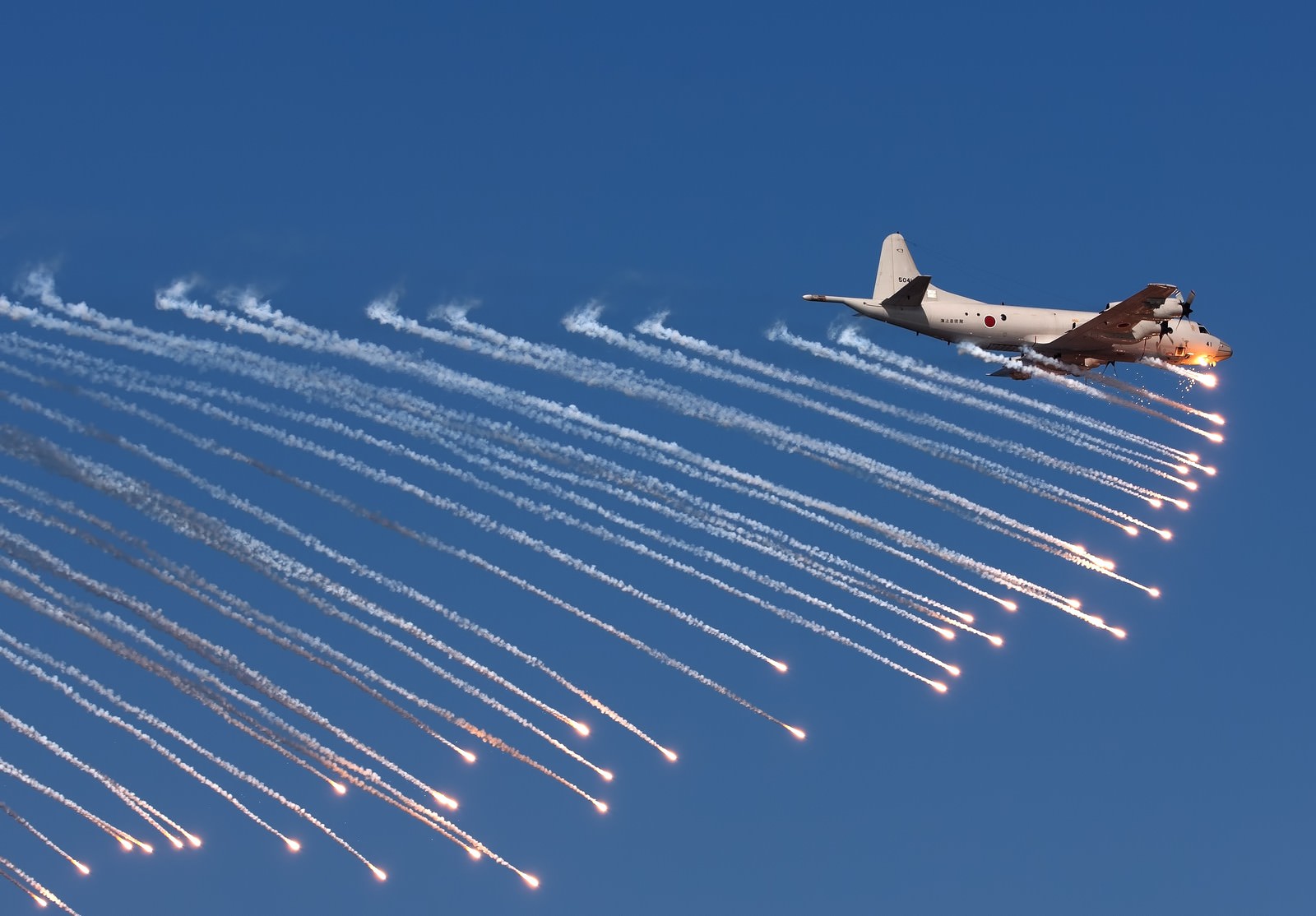 青空を飛ぶ戦闘機がフレアを放出する