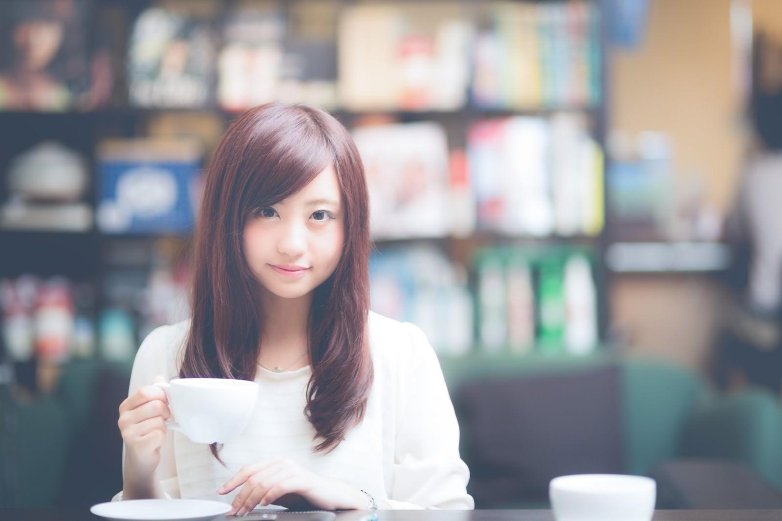 カフェで白いカップを持ち、微笑む白いシャツの女性［モデル：河村友歌］
