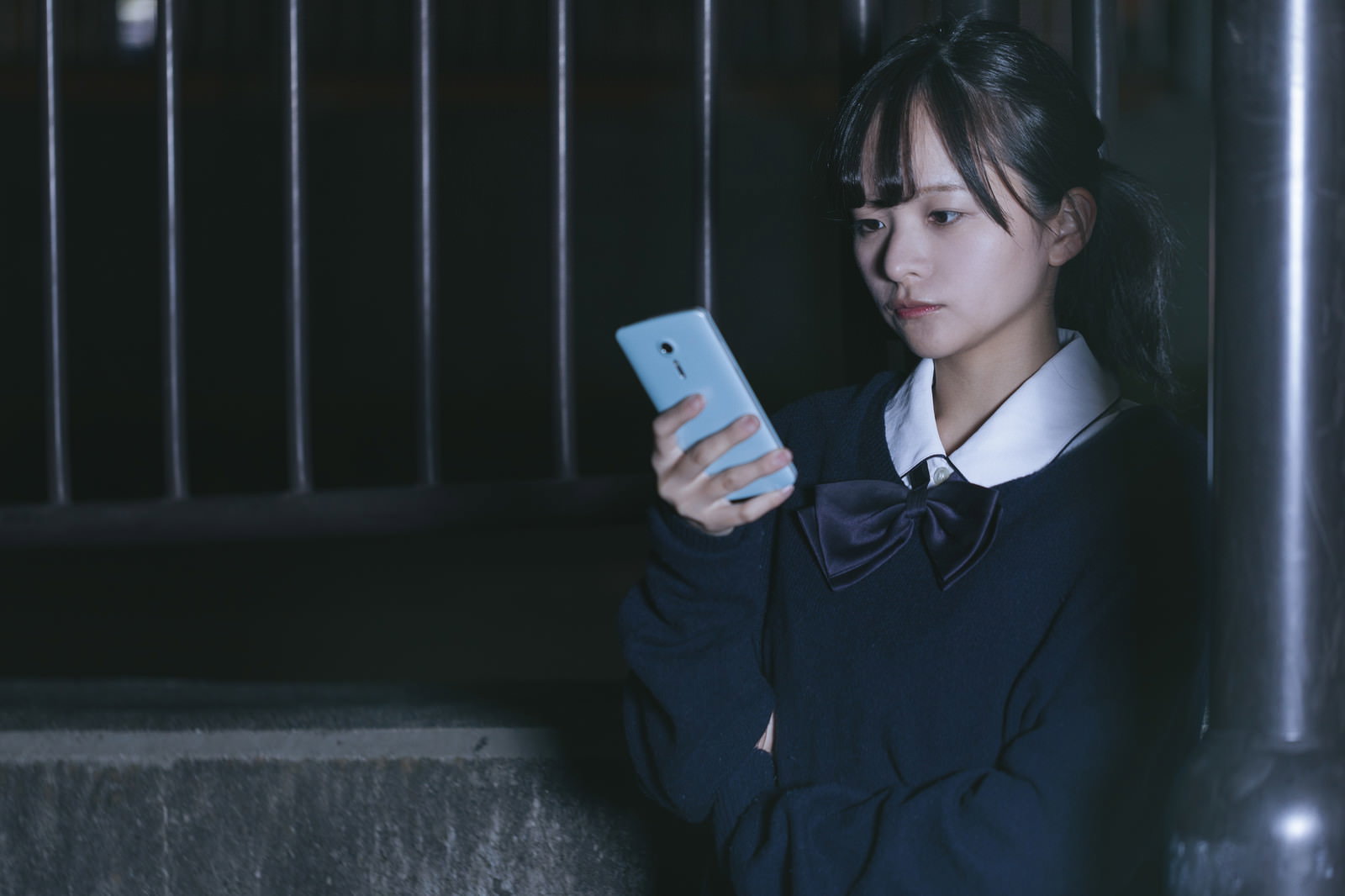 夜間の屋外でスマホを見る制服姿の女子高生［モデル：千歳］