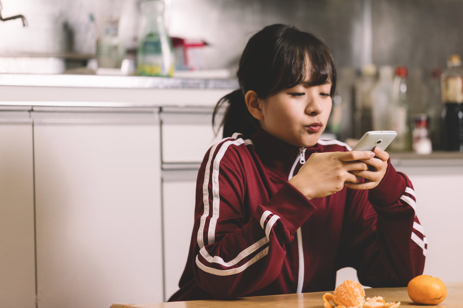 キッチンでスマホを見るジャージ姿の女の子［モデル：千歳］