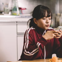 キッチンでスマホアプリに夢中なジャージ姿の女子の写真