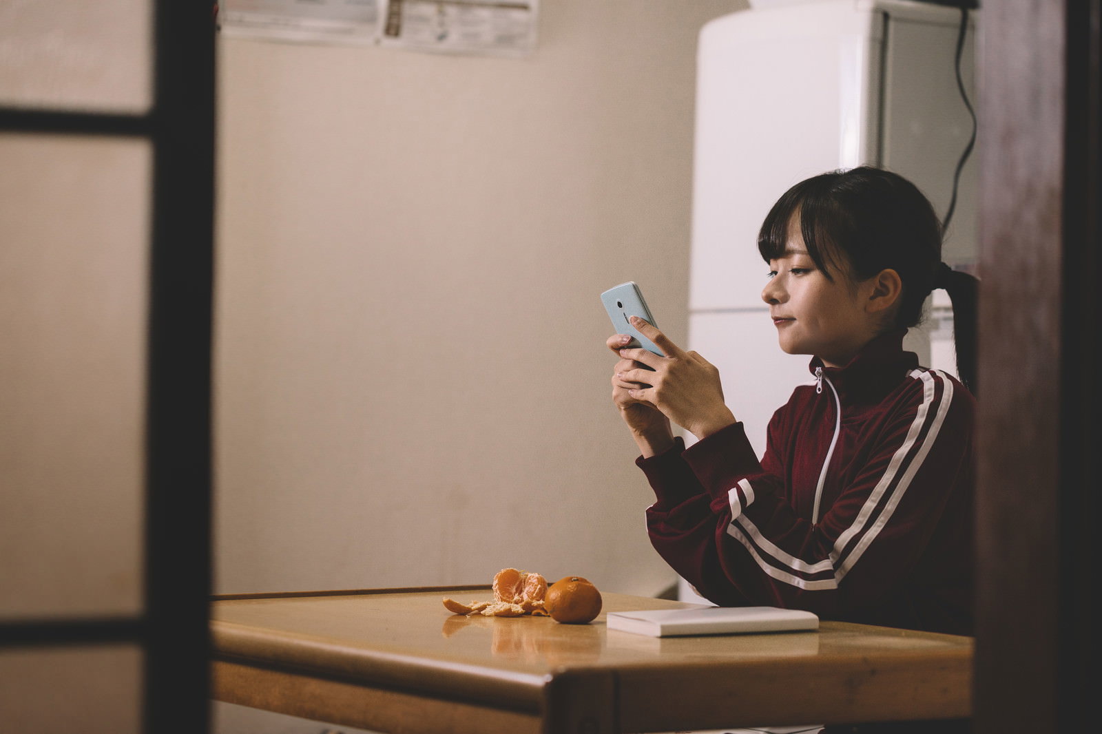 ジャージの女性がテーブルでスマートフォンを見ている［モデル：千歳］