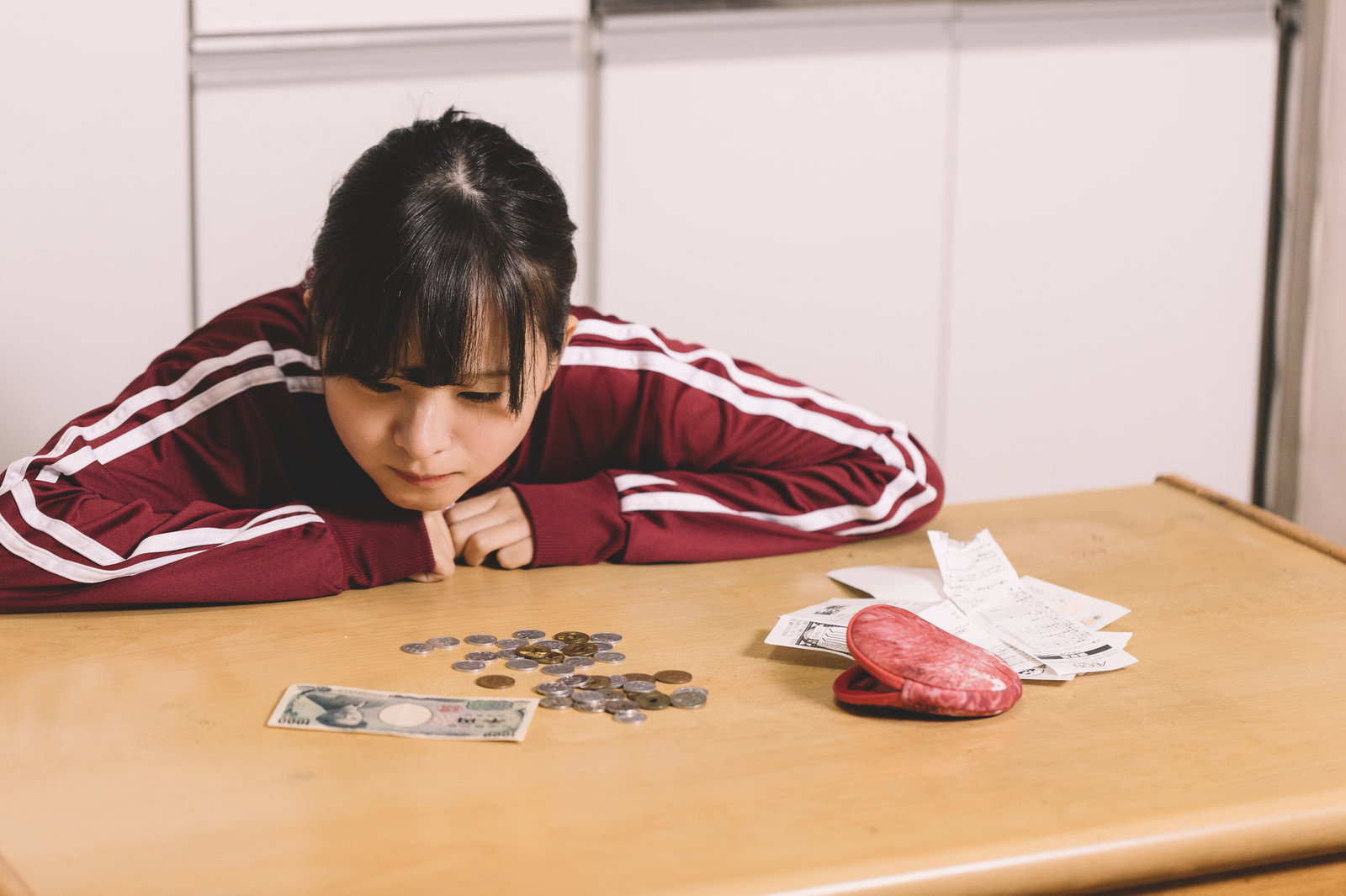 ジャージの女性が机でお金を数える［モデル：千歳］
