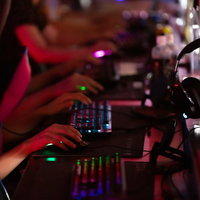 赤い照明が映るeスポーツ施設でPCゲームをするプレイヤーの手元の写真