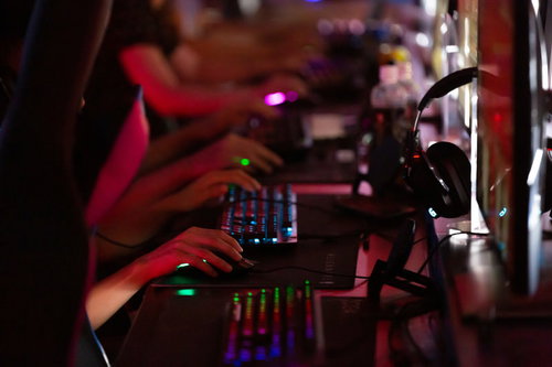 赤い照明が映るeスポーツ施設でPCゲームをするプレイヤーの手元