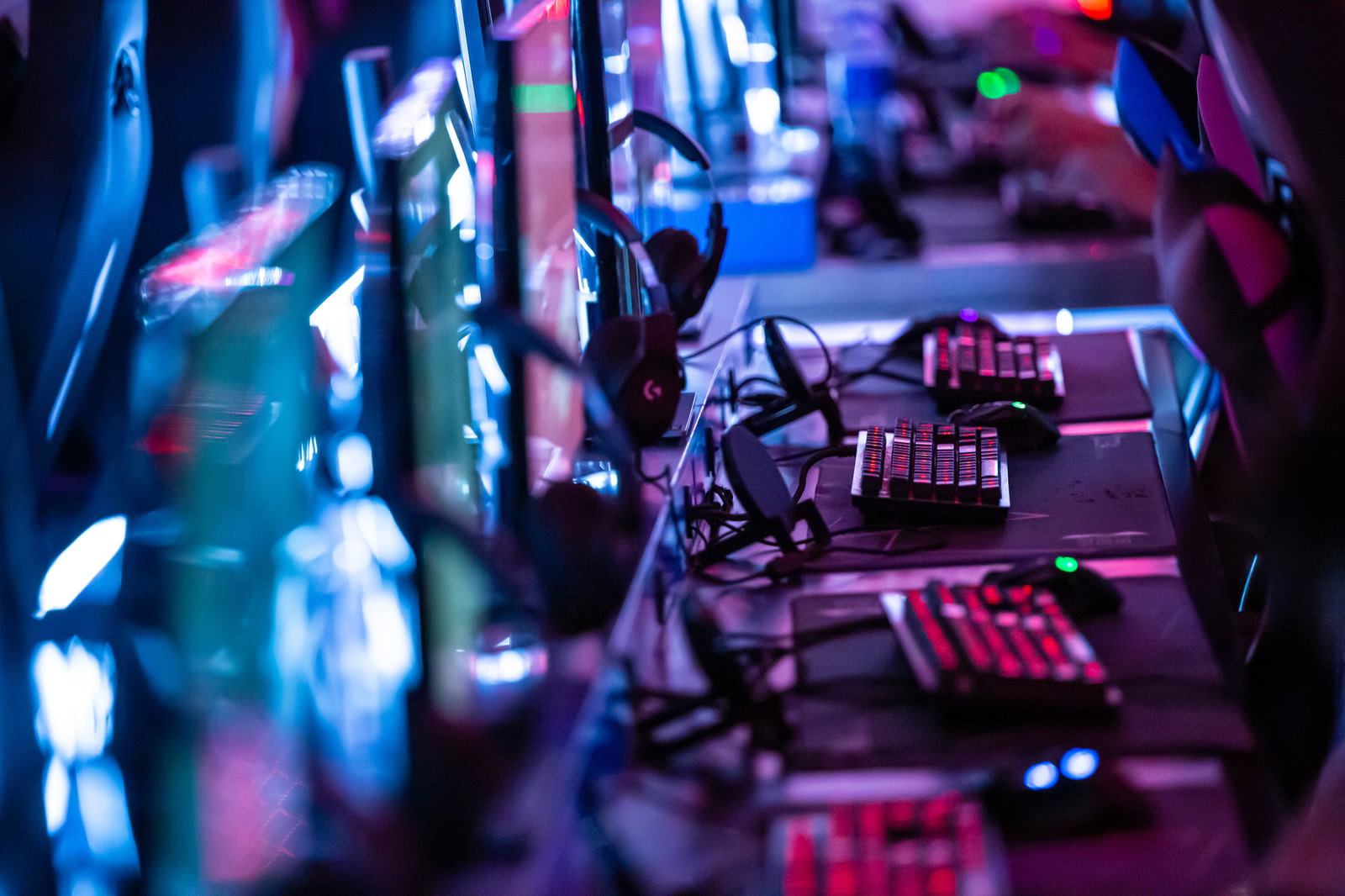 紫とピンクのネオンライトに照らされたゲーミングキーボードが並ぶeスポーツ施設
