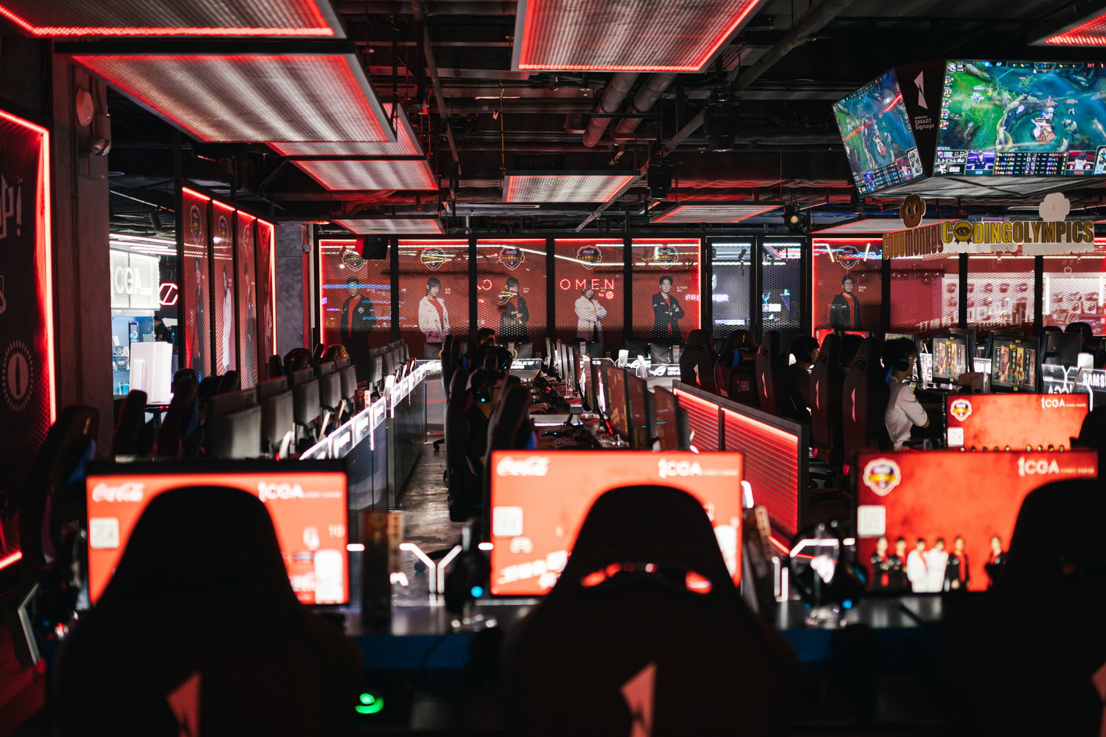 赤い照明に照らされたeスポーツ施設で複数のモニターとキーボードが並んでいる様子