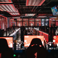 赤い照明に照らされたeスポーツ施設の複数モニターの写真