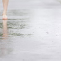雨が降りはじめる水たまりを歩く足元の靴と反射の写真